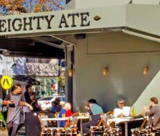 88cafe Outdoor cafe with diners at tables along a sunlit sidewalk under a beige awning.