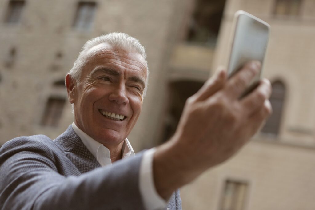 pexels-photo-3782193-3782193 - North Sydney Orthodontics Happy senior man smiling while taking a selfie with a smartphone outdoors.