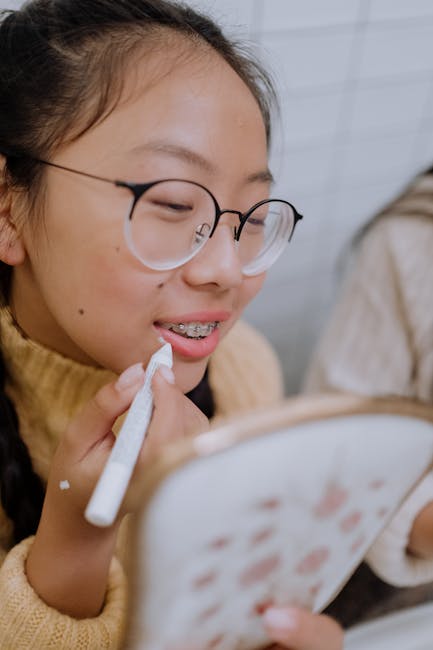 pexels-photo-5999355-5999355 - North Sydney Orthodontics Teen girl with glasses applies lipstick while looking in a mirror, showcasing beauty routine.